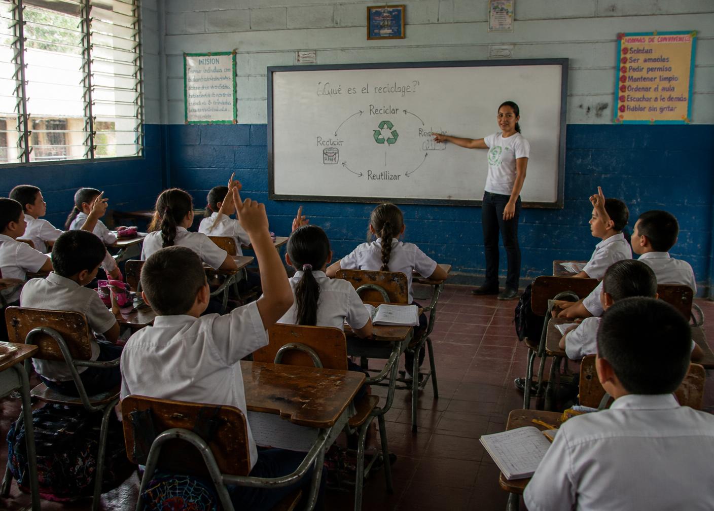 A teacher explaining a recycling diagram to a full class of Salvadoran primary students